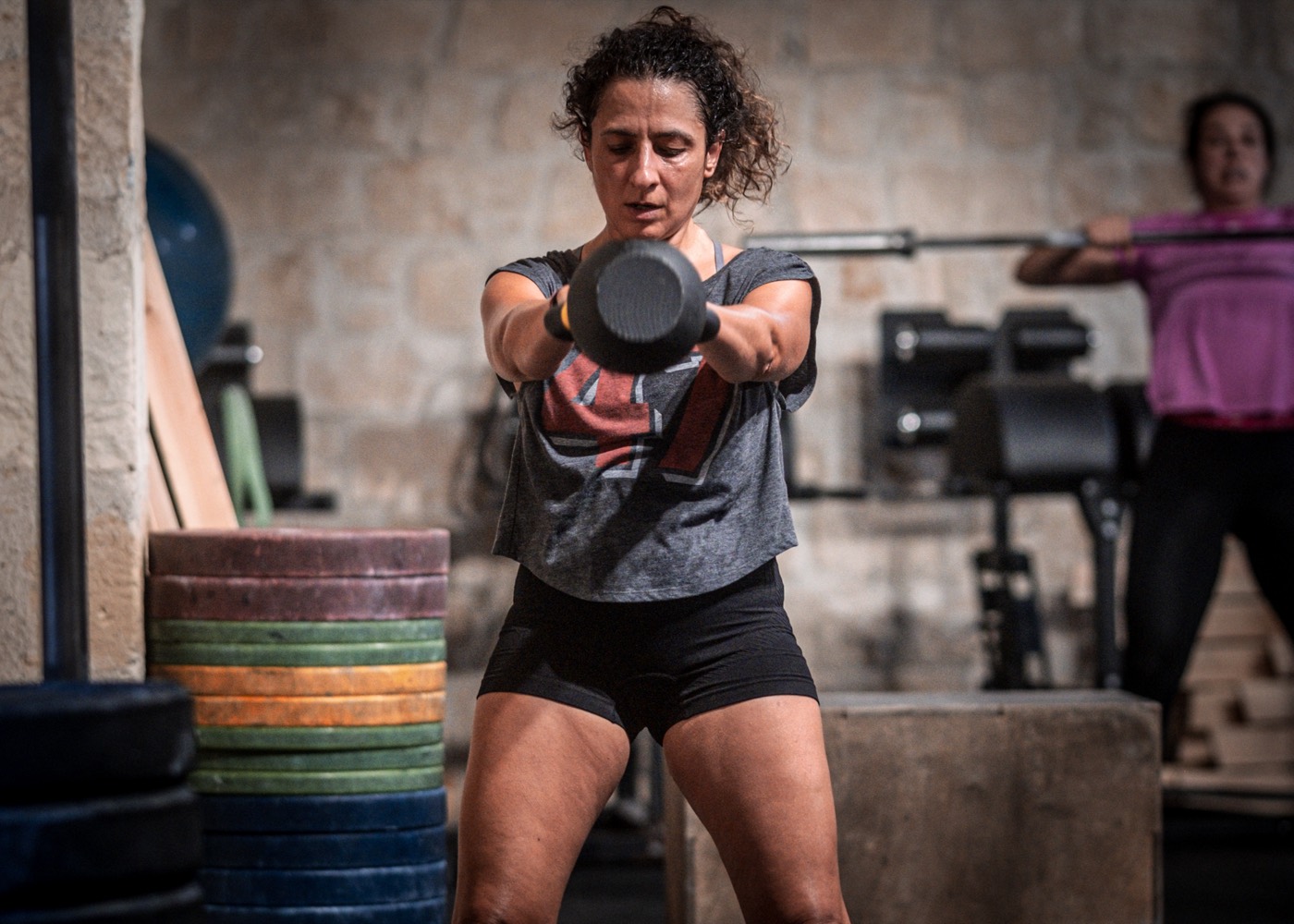 A member mid kettlebell swing in a class, another athlete training behind her.